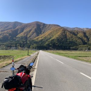 紅葉づいた北アルプスの山際に真っすぐ向かっていくロードにて
